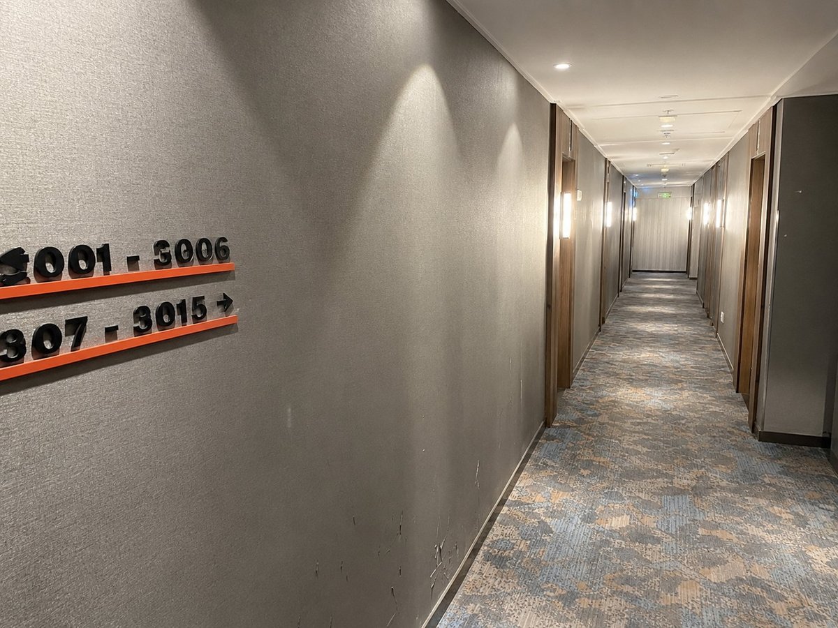 Long hotel corridor with beige walls, room number signs, and recessed ceiling lights leading down the hallway