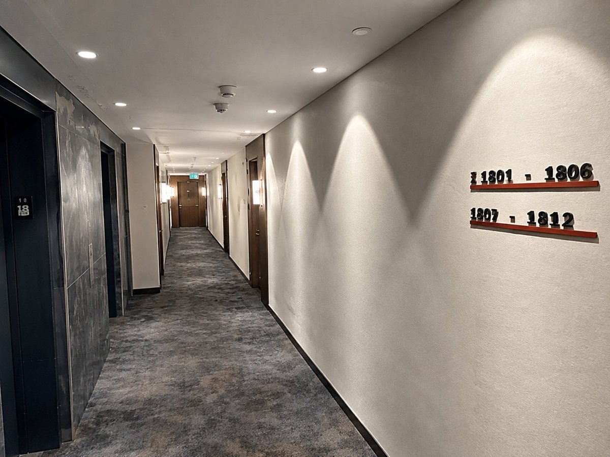 Modern hotel corridor with room numbers on white wall and recessed lighting