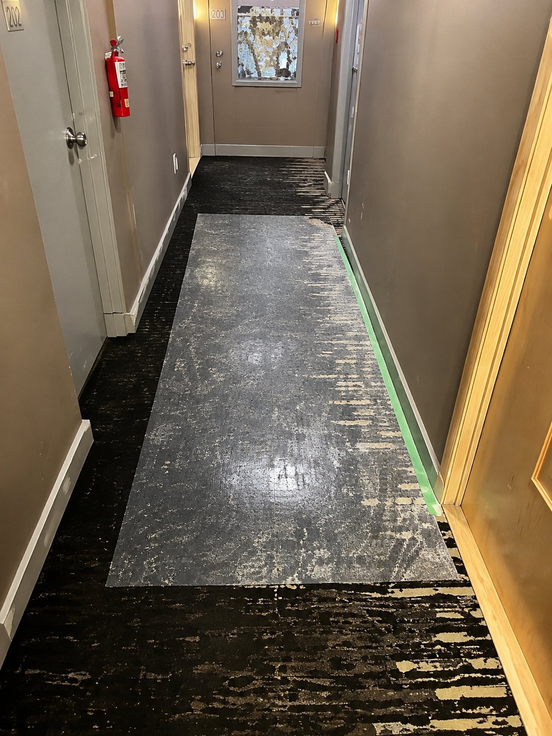 A narrow hallway with two-tone flooring: black textured floor on the left side and gray vinyl mat in the center, with a green edge trim and white-painted walls